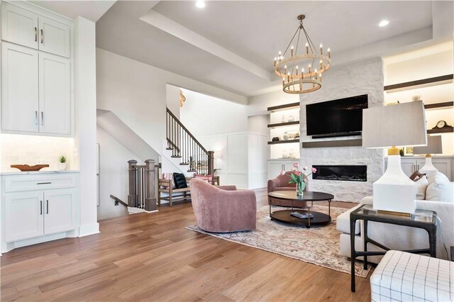 11594 S Zarda Dr, Olathe, KS 66061 - living room featuring a raised ceiling, light wood-style flooring, stairs, a premium fireplace, and a chandelier