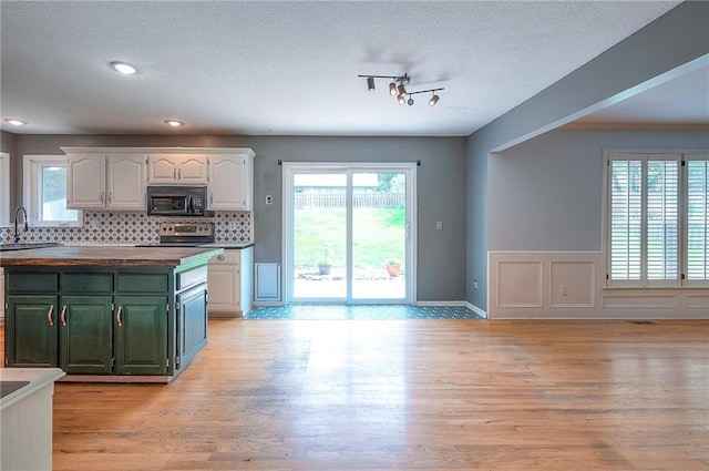9705 N Virginia Ave, Kansas City, MO 64155 - kitchen featuring black microwave, white cabinetry, stainless steel range oven, tasteful backsplash, and light wood finished floors
