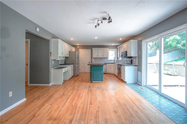 9705 N Virginia Ave, Kansas City, MO 64155 - kitchen with stainless steel appliances, light wood-style flooring, decorative backsplash, a textured ceiling, and a kitchen island