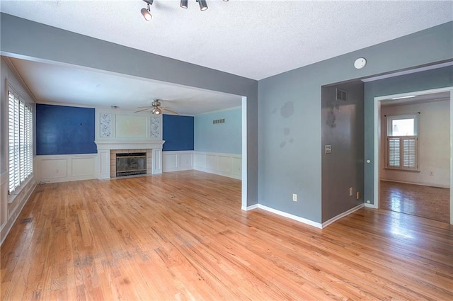 9705 N Virginia Ave, Kansas City, MO 64155 - unfurnished living room featuring ceiling fan, light wood-style flooring, a fireplace, wainscoting, and a decorative wall