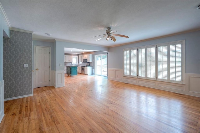 9705 N Virginia Ave, Kansas City, MO 64155 - unfurnished living room featuring crown molding, a textured ceiling, ceiling fan, a decorative wall, and light wood-type flooring