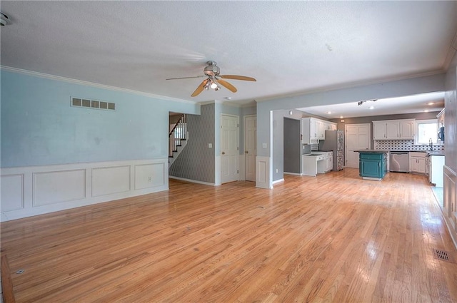 9705 N Virginia Ave, Kansas City, MO 64155 - unfurnished living room with crown molding, stairs, a ceiling fan, light wood-style floors, and a decorative wall