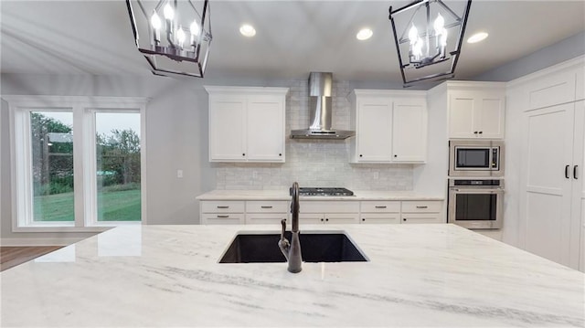22902 S Ridgeview Dr, Peculiar, MO 64078 - kitchen featuring appliances with stainless steel finishes, a chandelier, wall chimney exhaust hood, decorative backsplash, and white cabinets