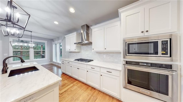22902 S Ridgeview Dr, Peculiar, MO 64078 - kitchen featuring stainless steel appliances, wall chimney range hood, a chandelier, light wood-type flooring, and white cabinets