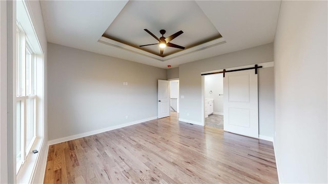 22902 S Ridgeview Dr, Peculiar, MO 64078 - unfurnished bedroom with a tray ceiling, a barn door, light wood-style floors, and ensuite bathroom