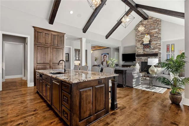 14713 Ash St, Leawood, KS 66224 - kitchen featuring beam ceiling, a kitchen bar, a center island with sink, light stone counters, and dark wood-style flooring