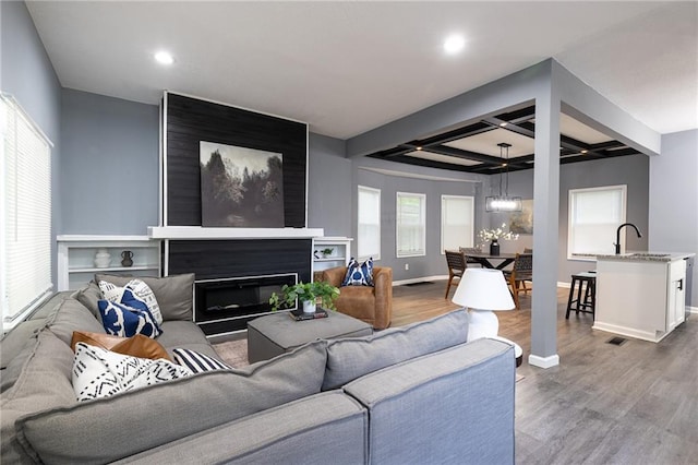 3428 College Ave, Kansas City, MO 64128 - living room featuring wood finished floors, coffered ceiling, beam ceiling, recessed lighting, and a glass covered fireplace