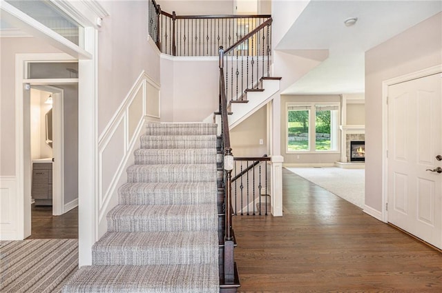 4824 W 162nd St, Overland Park, KS 66085 - staircase featuring a decorative wall, wood finished floors, a glass covered fireplace, a towering ceiling, and wainscoting
