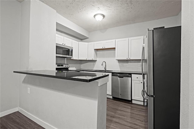 520 Sandusky Ave, Kansas City, KS 66101 - kitchen featuring stainless steel appliances, a peninsula, dark wood-style floors, white cabinetry, and tasteful backsplash