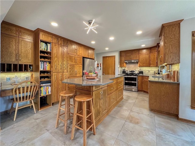 4117 NE Edgewater Ct, Lees Summit, MO 64064 - kitchen with appliances with stainless steel finishes, under cabinet range hood, tasteful backsplash, brown cabinets, and a kitchen island