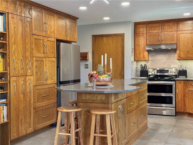 4117 NE Edgewater Ct, Lees Summit, MO 64064 - kitchen featuring appliances with stainless steel finishes, under cabinet range hood, brown cabinetry, tasteful backsplash, and a center island