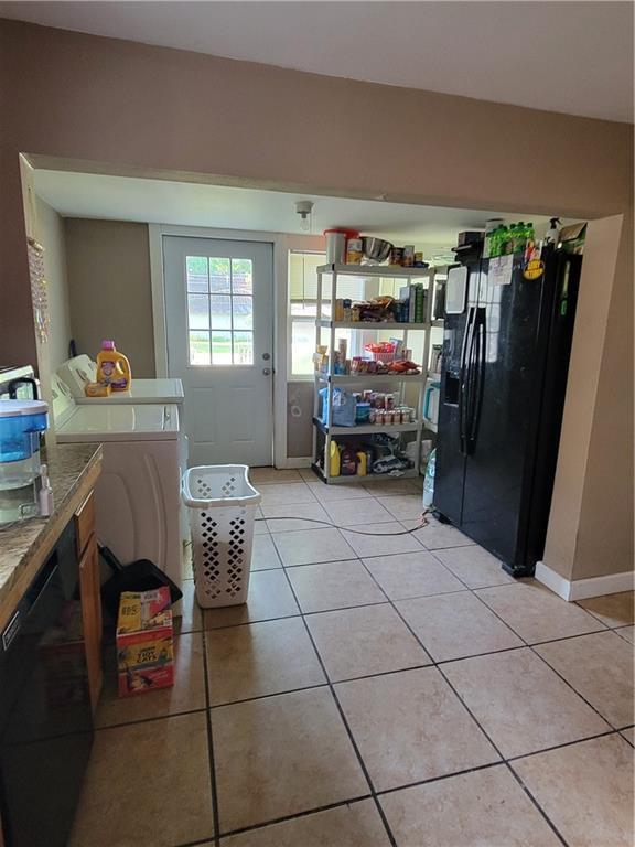 514 E Jackson Ave, Iola, KS 66749 - kitchen featuring black fridge, light tile patterned floors, and washing machine and clothes dryer