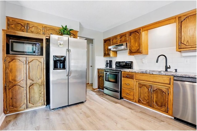 2541 NE Dale Hunter Ln, Lees Summit, MO 64086 - kitchen featuring stainless steel appliances, under cabinet range hood, light wood-style floors, tasteful backsplash, and brown cabinets
