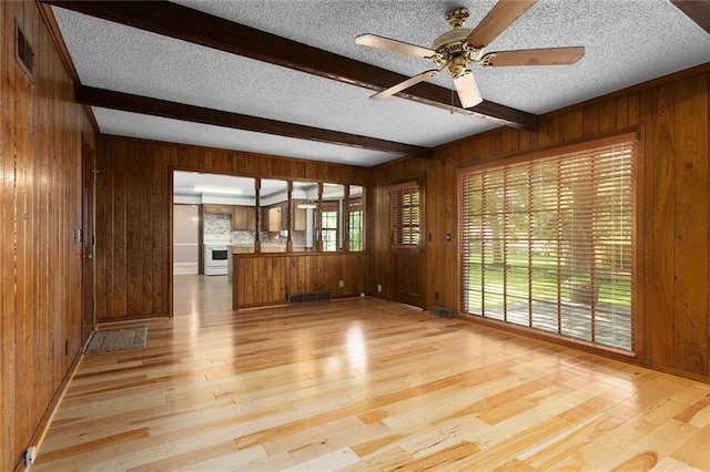 13220 W 76th St, Lenexa, KS 66216 - unfurnished living room with wooden walls, beamed ceiling, light wood-style floors, a textured ceiling, and a ceiling fan