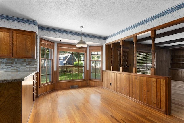 13220 W 76th St, Lenexa, KS 66216 - unfurnished dining area featuring wallpapered walls, light wood-style flooring, a textured ceiling, plenty of natural light, and wood walls