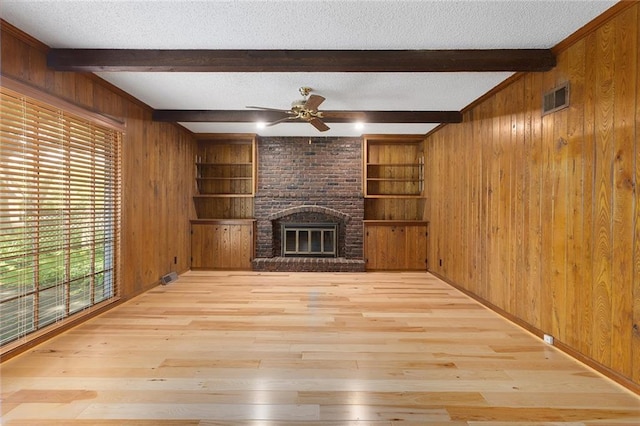 13220 W 76th St, Lenexa, KS 66216 - unfurnished living room with wooden walls, ceiling fan, wood finished floors, beamed ceiling, and a brick fireplace