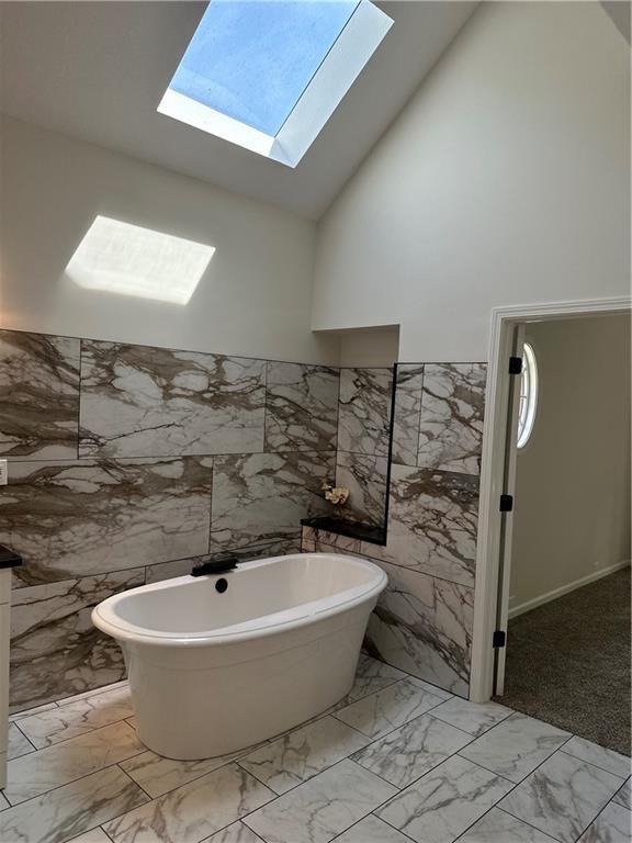 1411 NE 85th Ter, Kansas City, MO 64155 - bathroom with tile walls, a skylight, a freestanding bath, marble finish floors, and high vaulted ceiling
