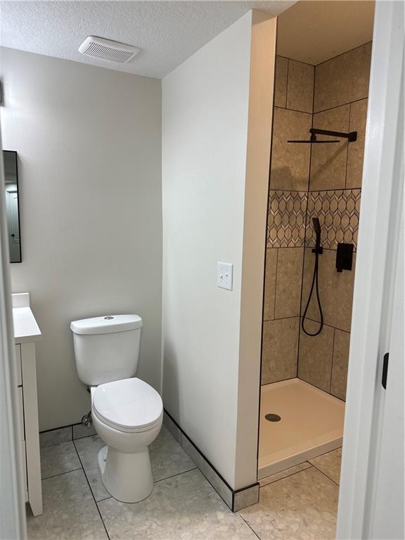 1411 NE 85th Ter, Kansas City, MO 64155 - full bathroom with vanity, a tile shower, a textured ceiling, and tile patterned flooring