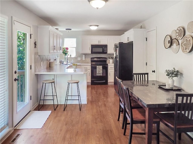 4301 NE 84th Ter, Kansas City, MO 64156 - kitchen with black appliances, a peninsula, light wood-style floors, white cabinetry, and light countertops