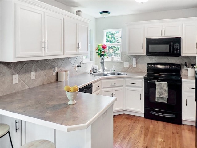 4301 NE 84th Ter, Kansas City, MO 64156 - kitchen with black appliances, a peninsula, white cabinetry, a breakfast bar, and light wood-style floors