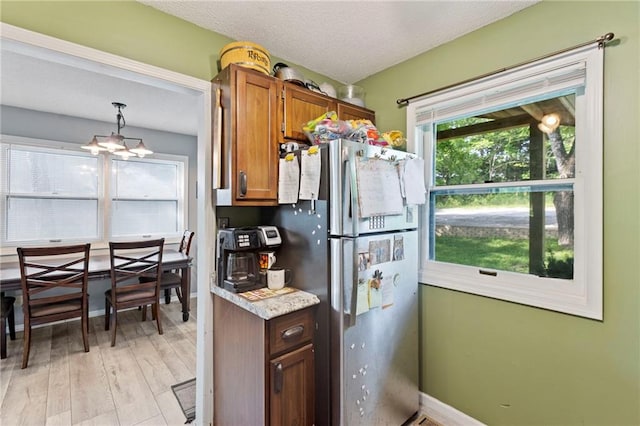321 W Sugarlake Dr, Mound City, KS 66056 - kitchen featuring freestanding refrigerator, light wood-style floors, brown cabinetry, light countertops, and hanging light fixtures