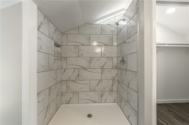 8801 E 49th St, Kansas City, MO 64129 - bathroom with tiled shower, a textured ceiling, vaulted ceiling, a spacious closet, and wood finished floors