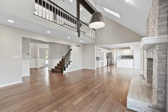 11412 Foster St, Overland Park, KS 66210 - unfurnished living room featuring high vaulted ceiling, a skylight, wood finished floors, stairs, and a fireplace
