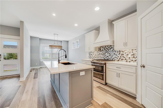 23506 E 10th St S, Independence, MO 64056 - kitchen featuring range with two ovens, premium range hood, backsplash, light wood finished floors, and an island with sink
