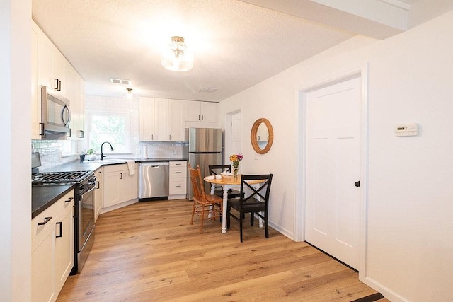 319 E 12th St, Ottawa, KS 66067 - kitchen with stainless steel appliances, light wood finished floors, backsplash, white cabinets, and dark countertops