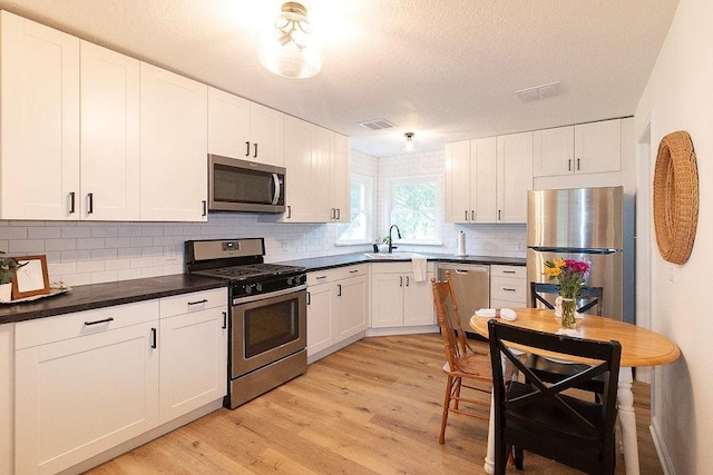 319 E 12th St, Ottawa, KS 66067 - kitchen with appliances with stainless steel finishes, light wood-style floors, white cabinetry, backsplash, and a textured ceiling