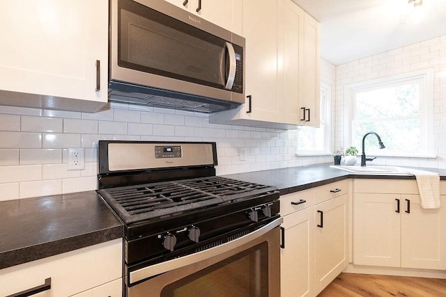 319 E 12th St, Ottawa, KS 66067 - kitchen featuring appliances with stainless steel finishes, dark countertops, decorative backsplash, light wood-type flooring, and white cabinets