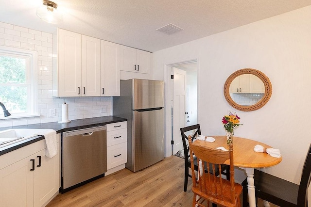 319 E 12th St, Ottawa, KS 66067 - kitchen featuring appliances with stainless steel finishes, light wood finished floors, backsplash, white cabinets, and dark countertops