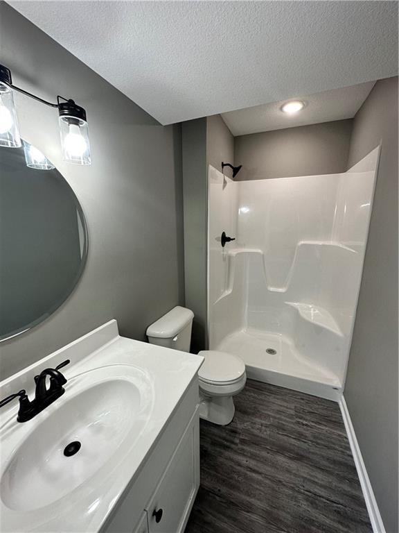 318 NE 51st Rd, Warrensburg, MO 64093 - full bathroom featuring a textured ceiling, wood finished floors, a shower, and vanity