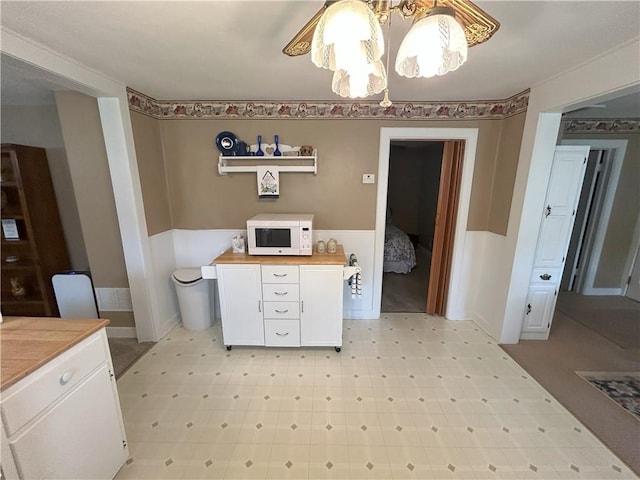 1047 N Lynn St, Nevada, MO 64772 - kitchen featuring white microwave, white cabinetry, a wainscoted wall, light flooring, and a chandelier