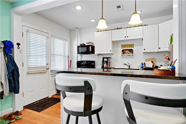 212 Emanuel Cleaver Ii Blvd Unit 2West, Kansas City, MO 64112 - kitchen with range, a breakfast bar, black microwave, white cabinetry, and recessed lighting