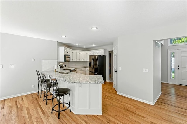 503 Amesbury Dr, Smithville, MO 64089 - kitchen with refrigerator with ice dispenser, a peninsula, black microwave, a kitchen bar, and light wood-style flooring