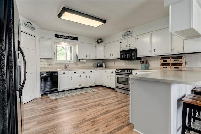 2450 Labette Rd, Ottawa, KS 66067 - kitchen with black appliances, a peninsula, light wood-style flooring, tasteful backsplash, and white cabinets