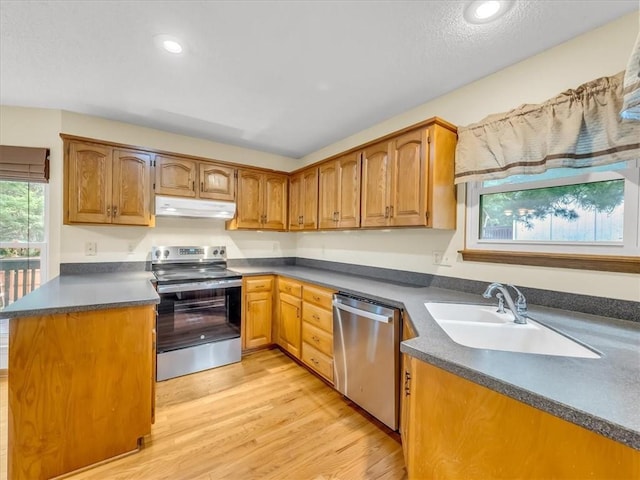 15409 Conser St, Overland Park, KS 66223 - kitchen with stainless steel appliances, under cabinet range hood, dark countertops, light wood-type flooring, and brown cabinetry