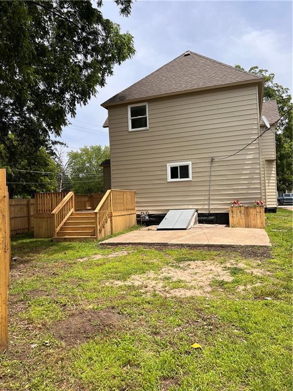 112 N High St, Butler, MO 64730 - rear view of house with a yard, a deck, a shingled roof, and stairway
