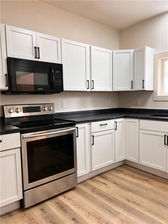 112 N High St, Butler, MO 64730 - kitchen featuring stainless steel electric range oven, black microwave, a textured ceiling, dark countertops, and light wood-style floors