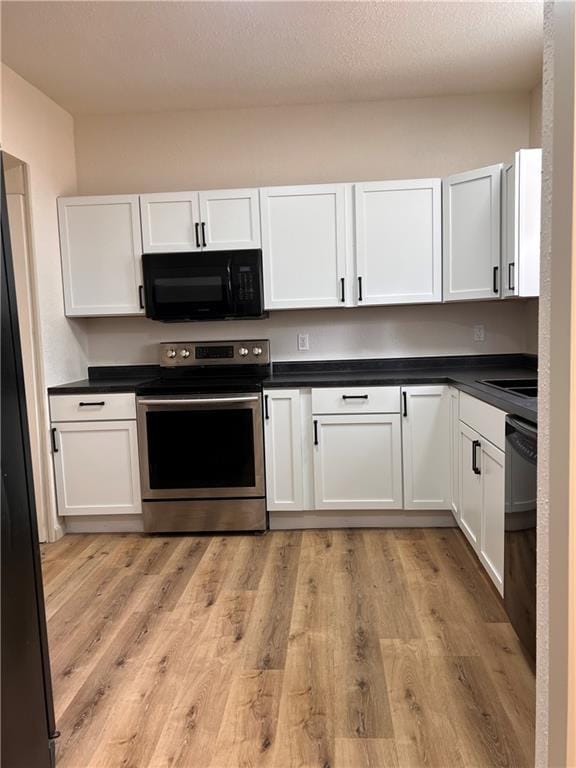 112 N High St, Butler, MO 64730 - kitchen with black appliances, white cabinetry, dark countertops, and light wood-style floors