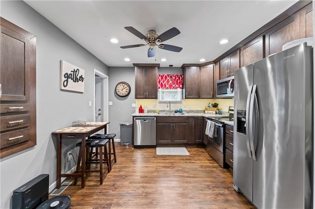 505 S Magdalena St, Concordia, MO 64020 - kitchen with appliances with stainless steel finishes, dark brown cabinetry, a ceiling fan, dark wood-style floors, and light stone counters