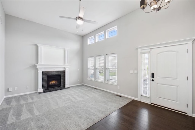 11704 N Laurel Ave, Kansas City, MO 64157 - unfurnished living room featuring a chandelier, a ceiling fan, wood finished floors, a fireplace, and a towering ceiling
