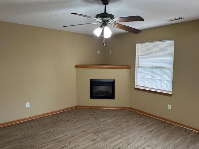 1002 NE Deer Creek Rd, Grain Valley, MO 64029 - unfurnished living room featuring a glass covered fireplace, wood finished floors, and ceiling fan
