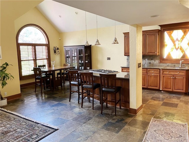 207 W 66th St, Kansas City, MO 64113 - kitchen featuring stone tile floors, stainless steel gas cooktop, lofted ceiling, brown cabinets, and pendant lighting