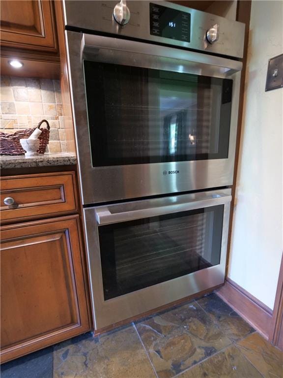 207 W 66th St, Kansas City, MO 64113 - kitchen view of double oven, brown cabinets, tasteful backsplash, and light stone countertops