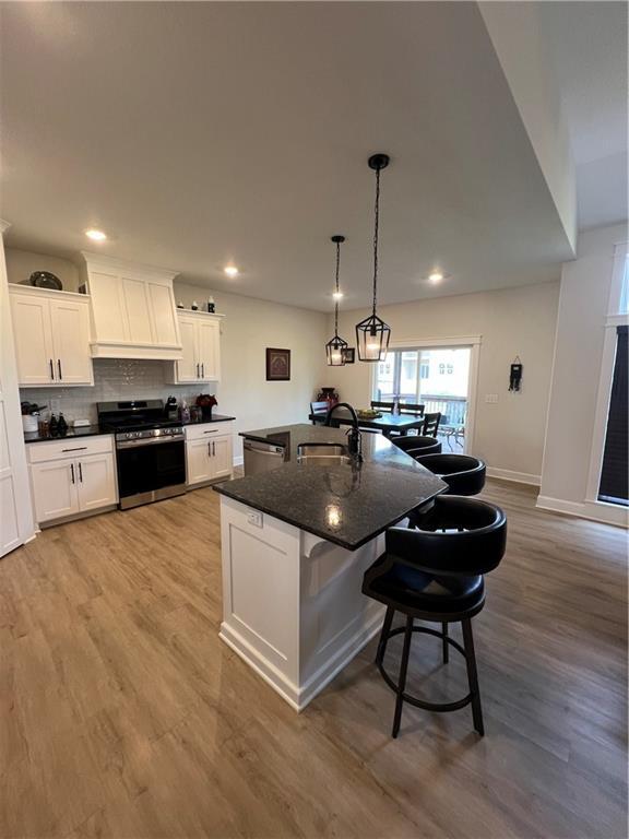 2321 Dovecott Dr, Kearney, MO 64060 - kitchen featuring stainless steel appliances, premium range hood, a kitchen breakfast bar, white cabinetry, and light wood-style floors