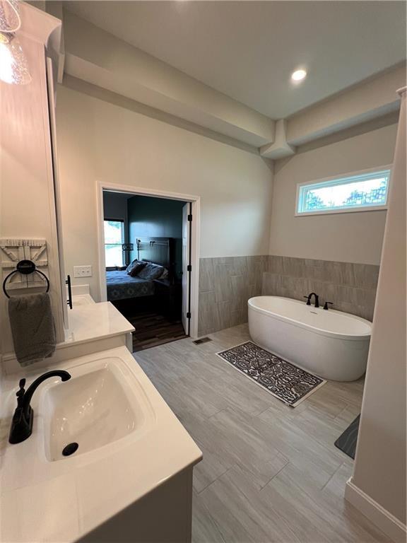 2321 Dovecott Dr, Kearney, MO 64060 - bathroom featuring vanity, a freestanding tub, tile walls, a wainscoted wall, and connected bathroom