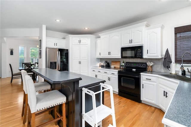 22833 W 44th St, Shawnee, KS 66226 - kitchen with black appliances, a breakfast bar, white cabinets, decorative backsplash, and light wood-style flooring