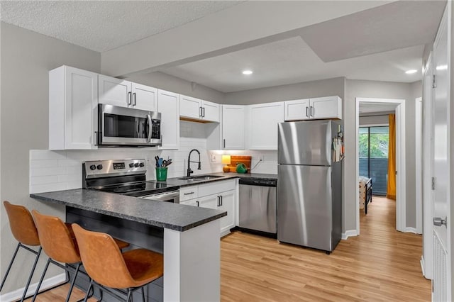 1509 W 25th Ct Unit A2, Lawrence, KS 66046 - kitchen featuring appliances with stainless steel finishes, dark countertops, a peninsula, light wood-style flooring, and recessed lighting
